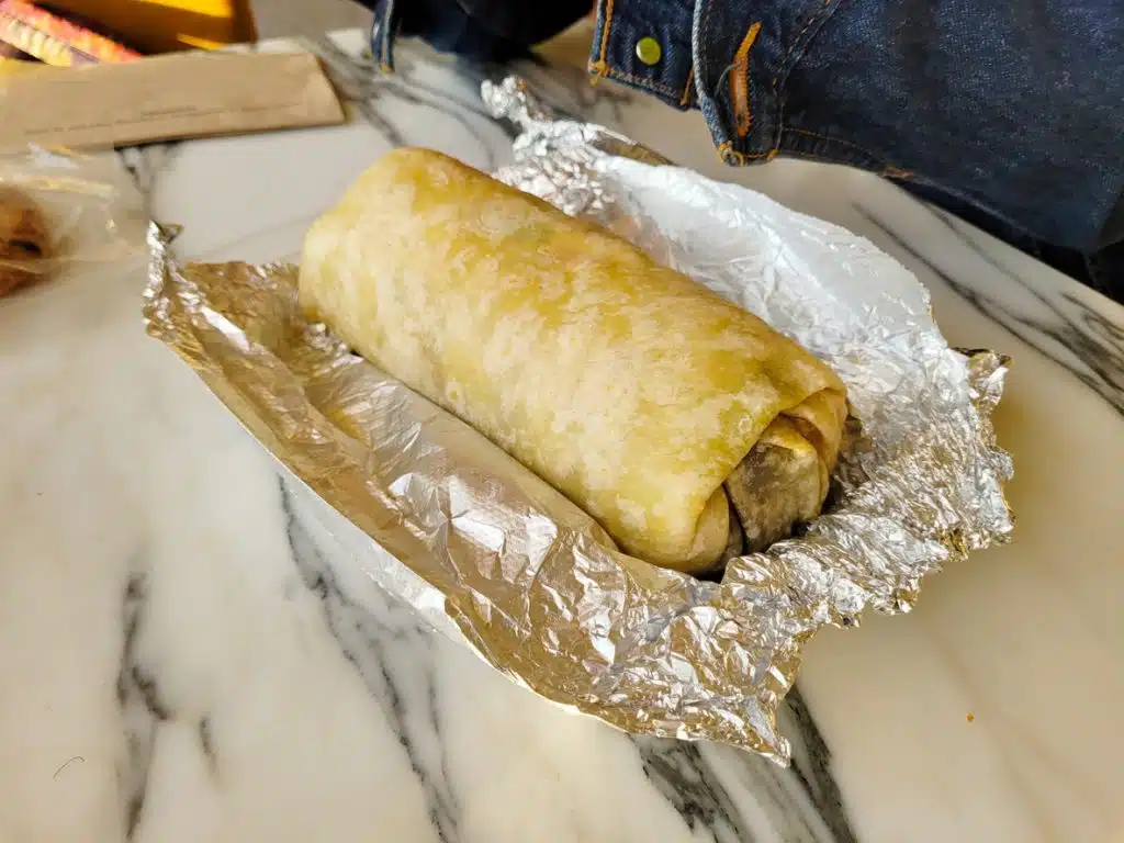 A freshly wrapped burrito in shiny tin foil from Esmeralda&rsquo;s 2.0 in Eureka, California &mdash; part of the Burrito Lunch Special where guests buy one burrito and get another plus a drink free. Authentic Mexican flavor and unbeatable value for Humboldt County locals.