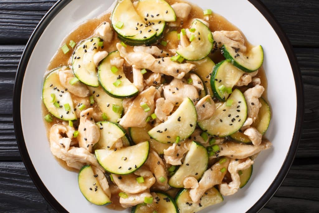 Tasty stewed chicken fillet with zucchini in spicy sauce close-up on a plate. Horizontal top view